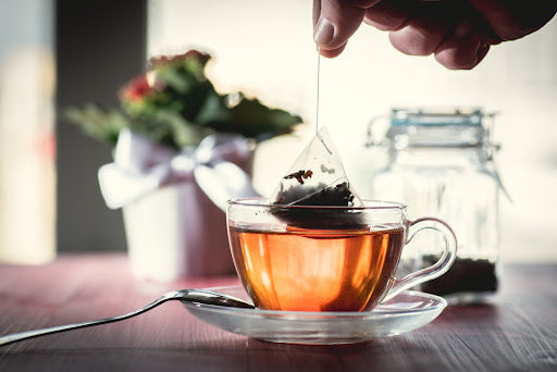 Tea bag being dipped into clear tea cup of water